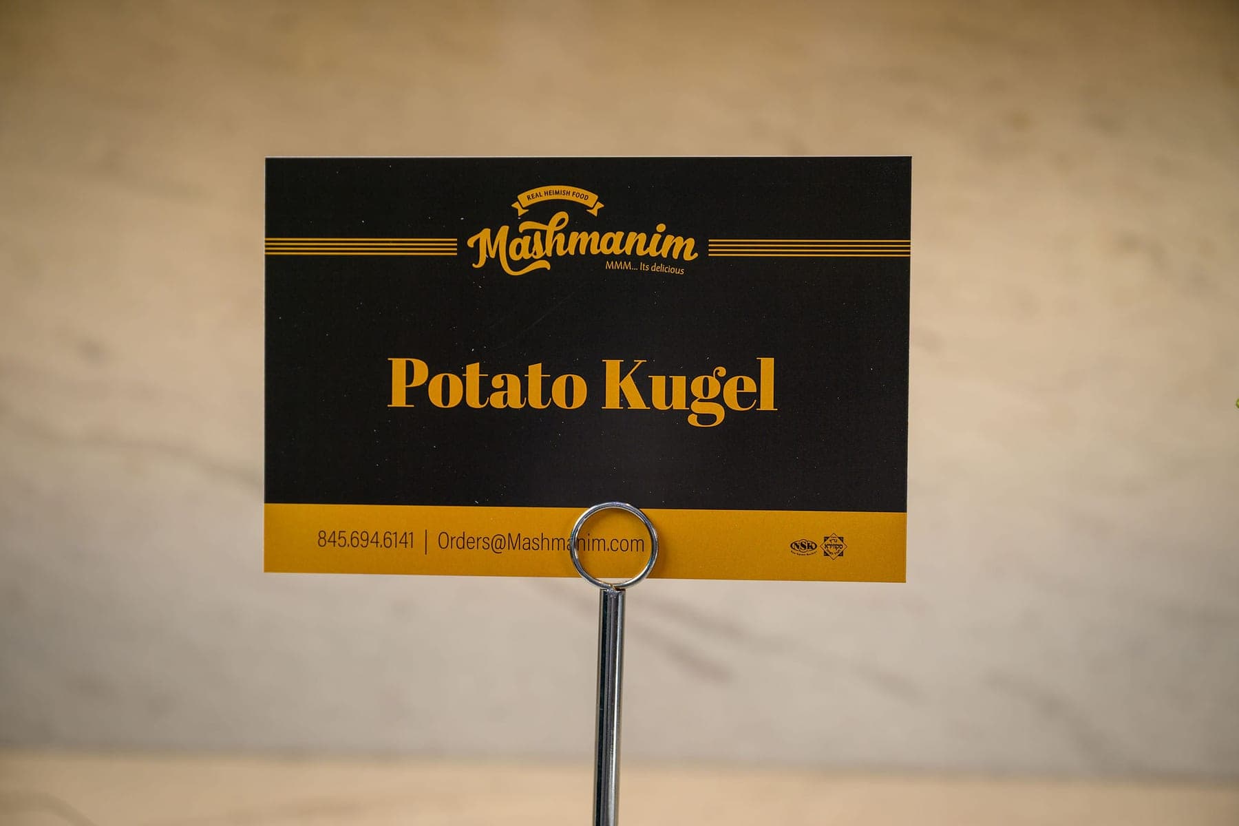A Mashmanim card reading Potato Kugel in gold on black, on its stand